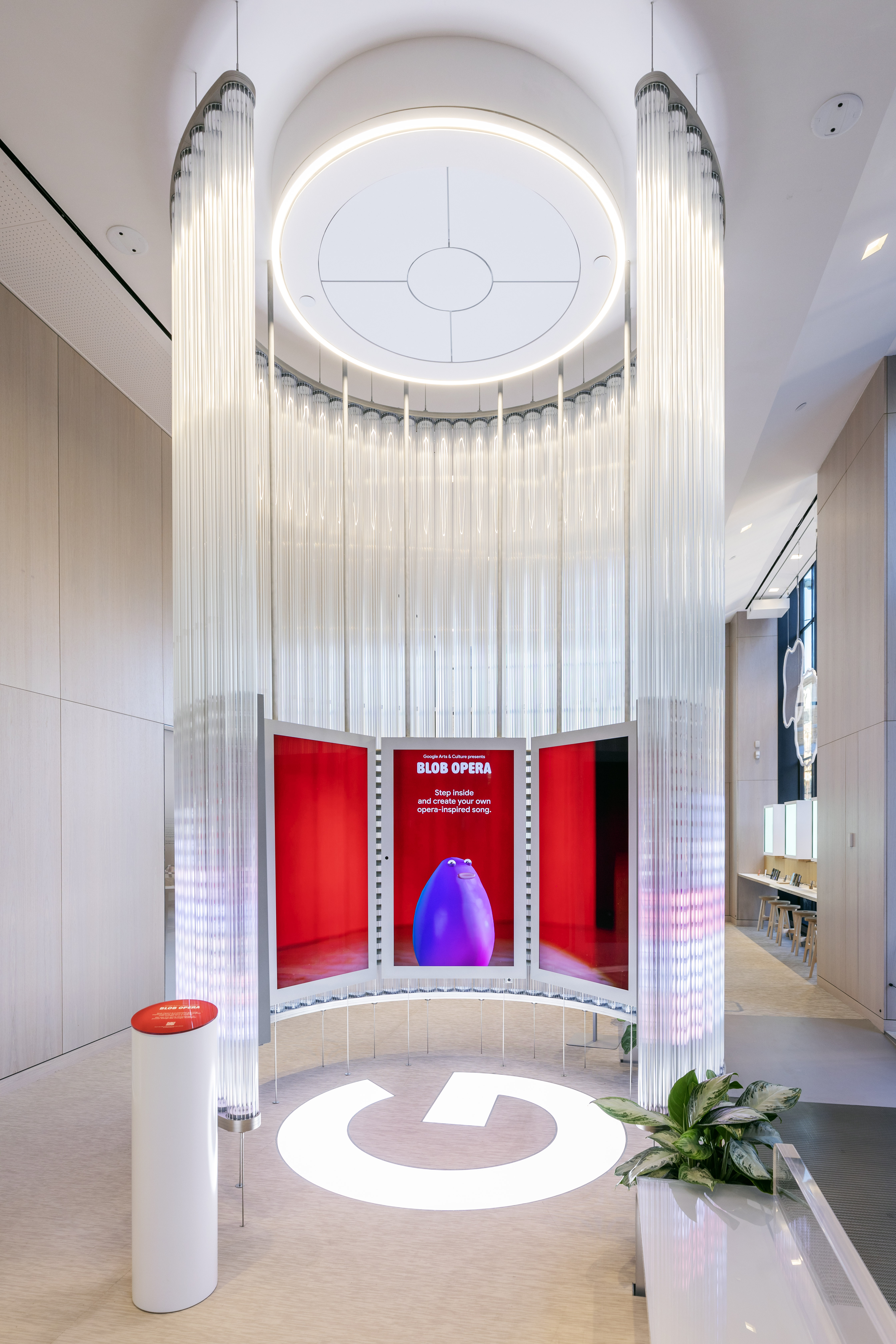 Final Blob Opera installation in ambient state inside the Google Store — a purple blob behind a triptych of red panels with 'Step inside and create your own opera-inspired song' messaging, surrounded by suspended glass tube columns