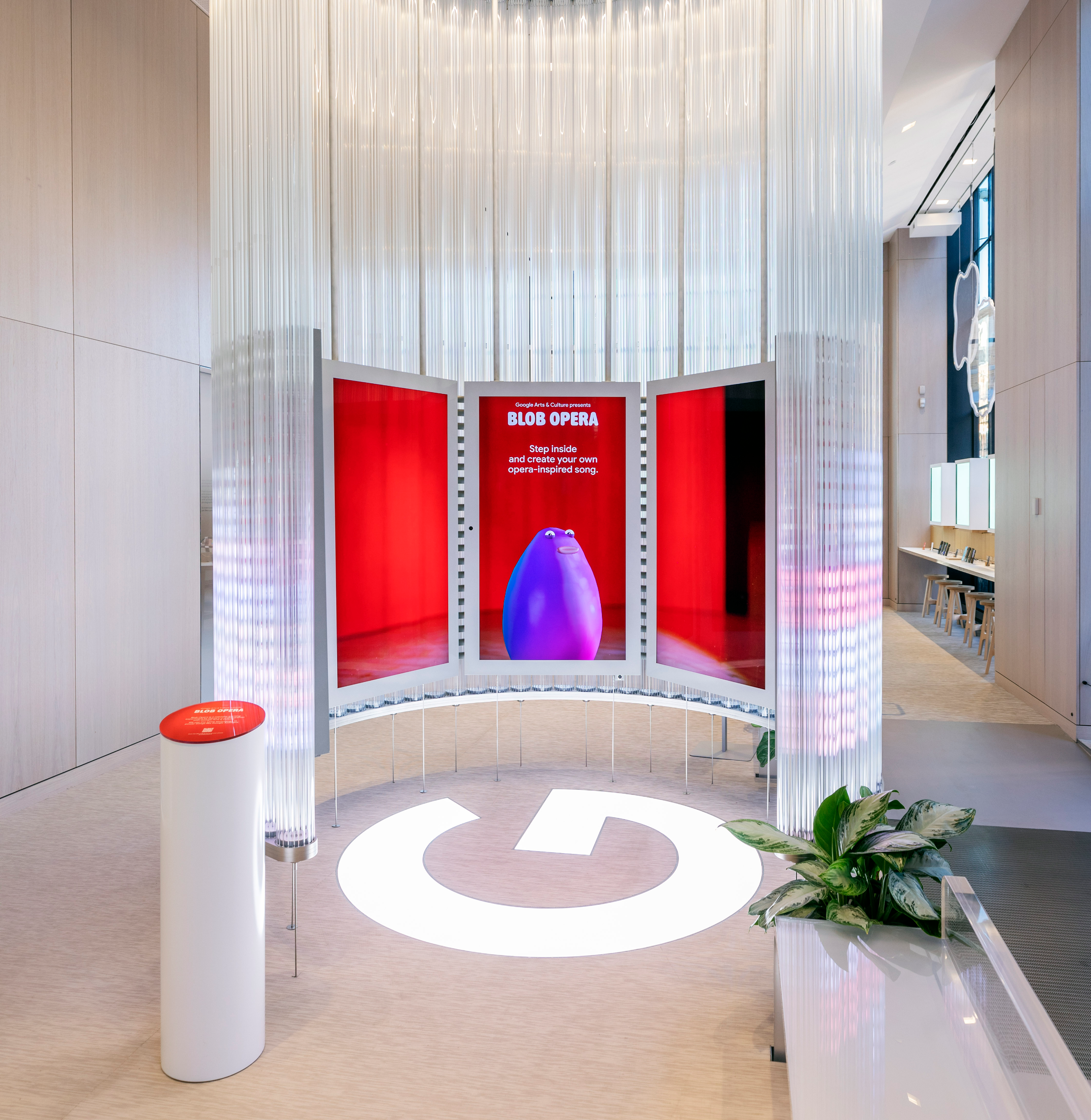 Google Blob Opera installation — purple blob character inside a red booth surrounded by suspended glass tube columns in the Google Store