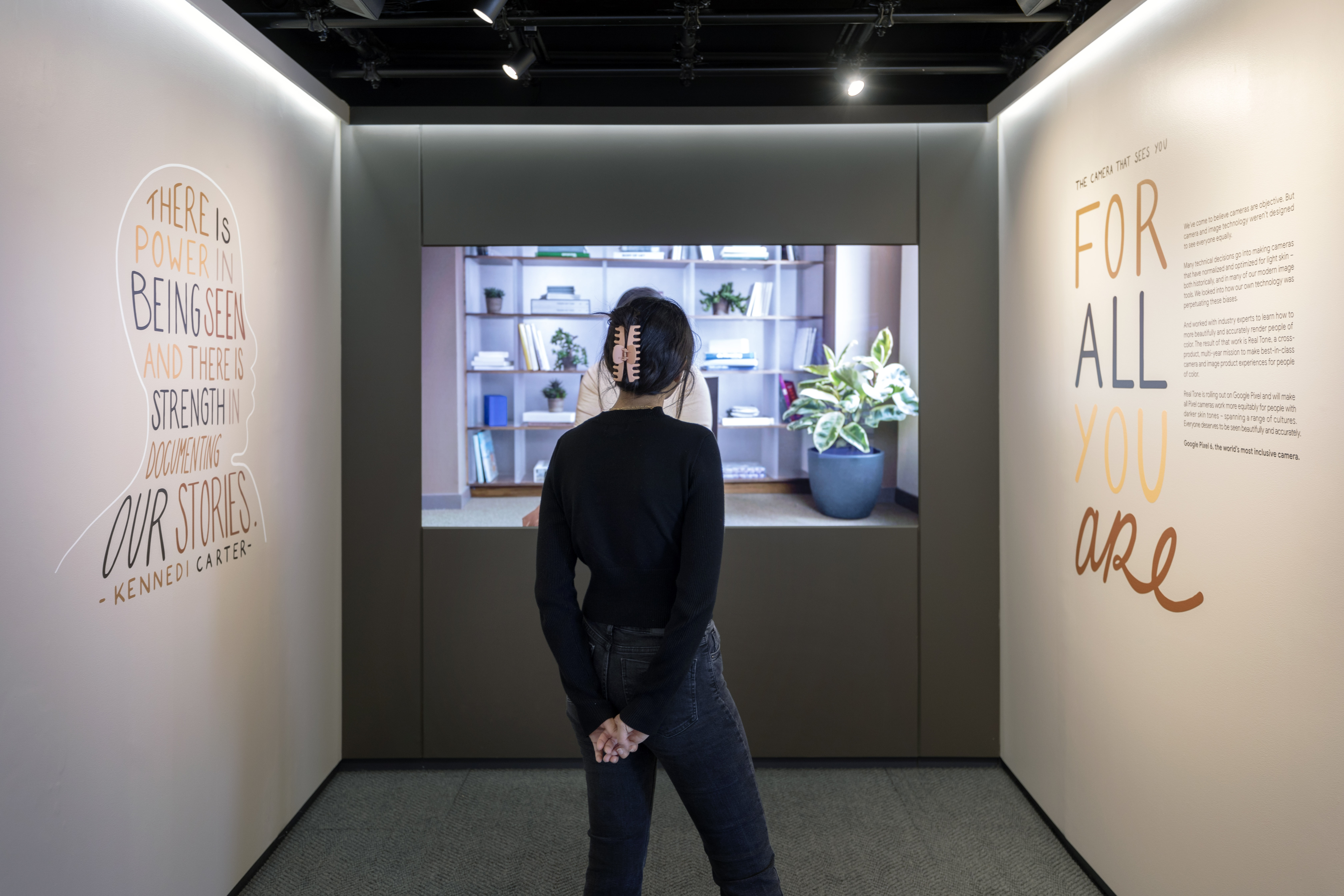 Back side of the Sandbox Room — guest viewing the Real Tone display flanked by the Kennedi Carter quote and the For All You Are campaign wall