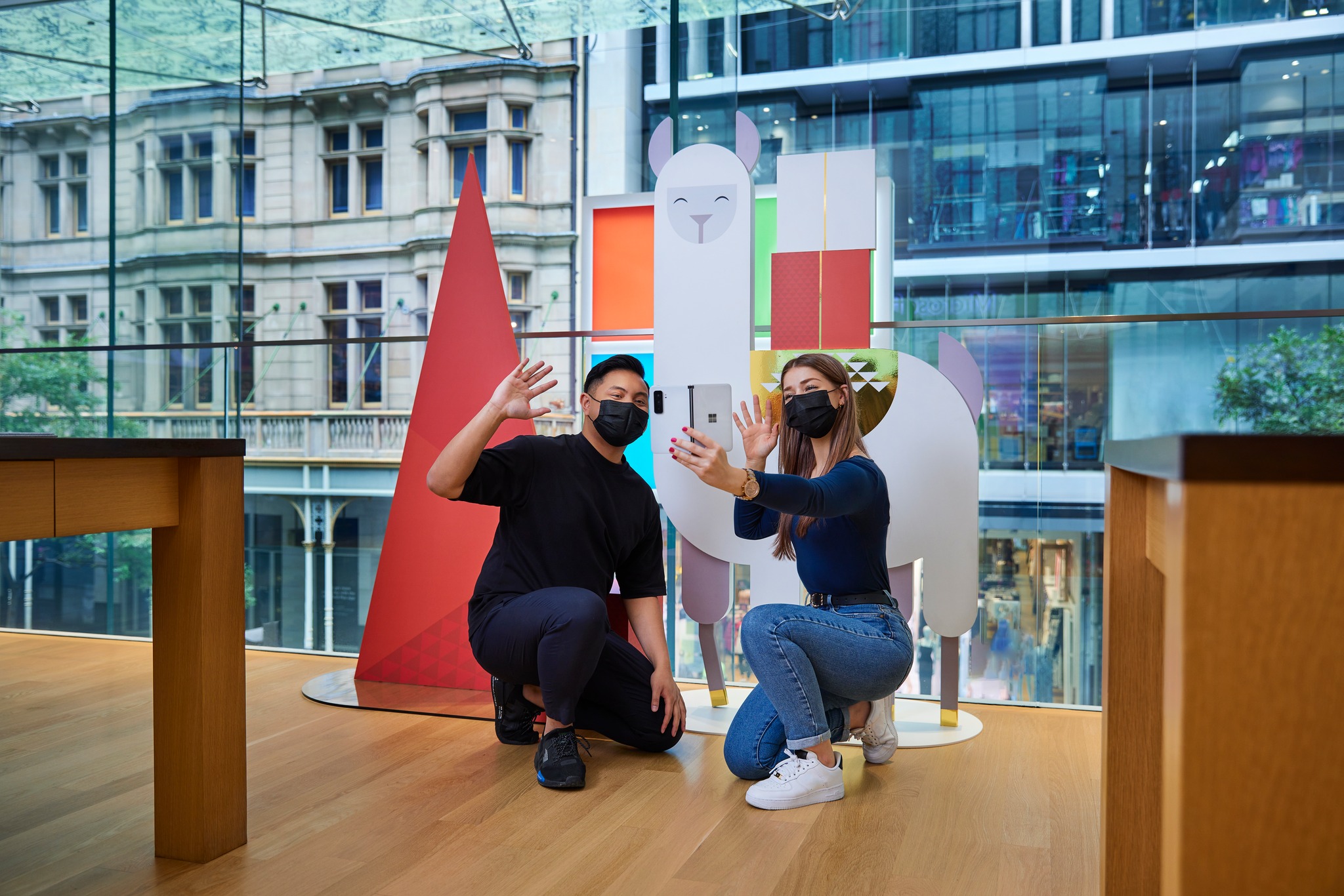 Microsoft holiday window display — customers taking a selfie in front of a llama holiday character installation in a Microsoft store